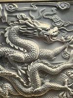 Close-up detail photo showing raised carving of a Chinese dragon's head and body with cloud motifs on black acrylic.