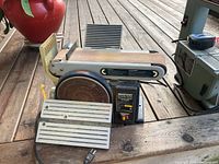View of the Mastercraft belt and disc sander showing sanding belt, disc, and metal work rests on the wooden deck surface.