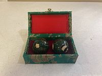 Pair of green Chinese hand balls inside their decorative green fabric-covered case with red lining.