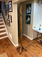 Full view of the wooden coat hanger standing on hardwood floor next to a staircase and wall with photos.
