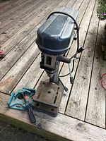 Side angle showing the drill press on a wood surface with attached lever and included angle guide accessory.