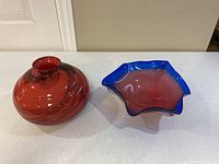 Red round vase and blue-red bowl displayed side by side on white surface.