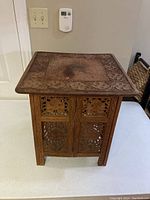 Front view of a square hand carved wooden folding table with detailed floral and geometric carvings and a stain in the center of the top surface.