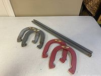Four metal horseshoes, two red and two gray, and two cylindrical metal posts on white surface
