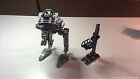 First Order AT-ST bipedal Lego walker model alongside a small stand accessory on white background showing overall build and scale.