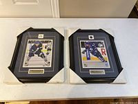 Photo showing two framed official NHL photos of Phil Kessel and Dion Phaneuf in protective corner covers, still wrapped.