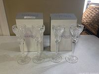 Photo showing two Marquis Waterford branded boxes behind four clear long stem glasses, arranged standing on a surface in natural light.