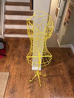 Full view of the yellow metal wire dress form display on wooden floor near stairs.