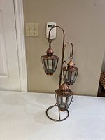 Front view of three-tiered outdoor patio lighting stand with three copper-tone lanterns hanging at different heights.