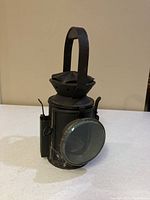 Front view of black metal railway lantern with handle and round glass lens on front door.
