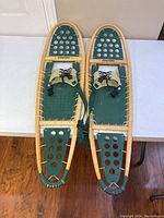 Top-down view of the pair of Winter Hiker snowshoes showing wooden frames, green decking with holes, and leather lace bindings.