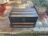 Front view of the vintage wooden chest showing alternating wood slats and black painted wood with metal corner and strap accents, metal latch on front.