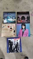 Five vinyl records laid out on floor, showing front covers of The Clash, Joan Jett, Rush, Asia, and World albums