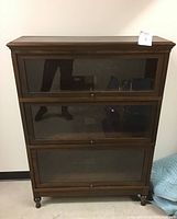 Front view of assembled four-piece bookcase showing three glass-door compartments and crown top, dark brown finish