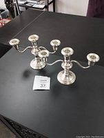 Two sterling silver candelabra candle holders displayed on a dark surface showing their overall shape and design.