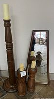 Full view of all items: tall candleholder, two rustic candleholders with candles, and triangular mirror leaning against wall.