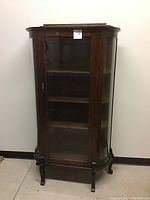 Full front view of the curved glass curio cabinet showing the wood frame, glass door and shelves inside.