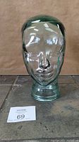 Front view of the transparent glass mannequin head showing detailed facial features and smooth glass surface.