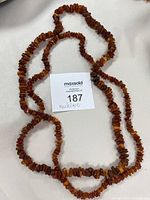 Long necklace of multi-coloured brownish beads shown laid flat on white surface, 31 inches in length.