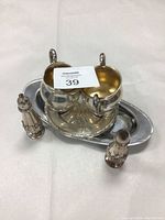 Sterling silver sugar and creamer set with handles and gold-toned interiors placed on an oval silver plated tray with beaded border, flanked by vintage silver plated salt and pepper shakers.