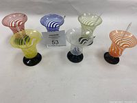 Overview of six multi-colored swirled glasses on black pedestal bases