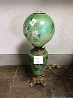 Full view of the green antique oil lamp showing floral painted globe and ornate brass base