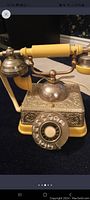 Close-up of silver-tone rotary dial telephone with yellow handset and detailed filigree metal base