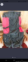 Front view of the black and red OUTBOUND camping backpack showing adjustable shoulder straps, two red mesh side pockets, and multiple compression straps.