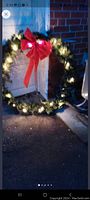 Photo of the wreath hung outside showing the illuminated white LED lights and red bow, demonstrating overall size and lighting effect.