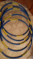 Five blue plastic dance hoops laid out on a beige floral bedspread, each wrapped partially with yellow grip tape, arranged showing size and detail.