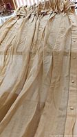 Drapes laid out showing the full length and texture of pale gold linen fabric with ruffles and buttons along the edge.