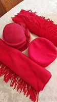 Photo of two red lambswool scarves and two red 100% wool hats on a floral tablecloth.