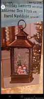 Box with image of bronze holiday lantern featuring snowman and Christmas tree inside, lit with LED light.