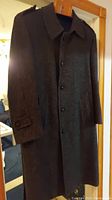 Front view of the dark wool men's winter coat hanging on a door.