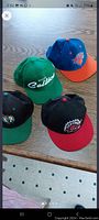 Four vintage NBA snapback baseball caps from Toronto Raptors, Boston Celtics (2), and New York Knicks teams arranged on wooden surface