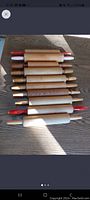 17 wooden rolling pins laid out flat on a wooden table, showing variation in handle color and wood tone.