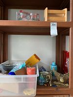 Shelf with brass eagle bookends, Wilton bowl, candles, and various glassware items shown together in a plastic container and on the shelf.