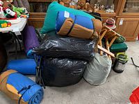 Stack of rolled air mattresses or sleeping pads in various colors with bags and camping chairs