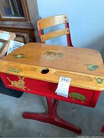 Full view of child's metal and wood school desk showing vintage animal decals on desk surface and front panel, with red metal frame and wooden chair.