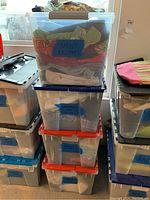 Four plastic bins stacked; top labeled Men's Clothes, middle labeled Women's Tops XL, bins filled with assorted clothing
