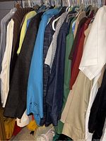 Photo showing variety of men's clothing hanging on rack including colorful pullovers, jackets, and dress shirts, various colors such as white, blue, brown, green, and red.