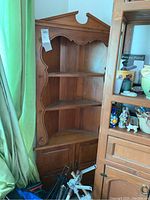 Full view of wood corner hutch showing three open shelves, decorative carved edges, and lower cabinet with two doors.