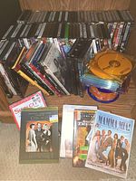 Photo showing a mixture of DVDs and CDs including Chicago, Mamma Mia!, and DVDs on spindles.