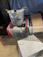 Three plastic storage bins filled with various electrical hardware items including lamps, cables, keyboards, and remotes.