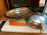 Stack of four silver plate serving dishes on top of plastic cutting boards and metal cookie sheet