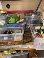 Wide view of multiple plastic bins filled with assorted hardware items such as tape, bulbs, small tools, and various components.