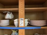 Photo of shelves holding stacks of plates, cups hanging, and other pieces showing the quantity and variety of the set