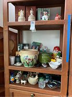 Wood shelving unit containing a variety of crocks, vases, plant pot, glass items and figurines including a clown toy and snow globe.
