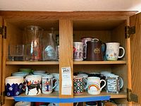 Full view of two wooden shelves displaying assorted mugs and glass vases.