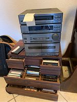 Full view of the stereo cassette deck receiver with multiple wooden drawers open containing numerous audio cassette tapes.